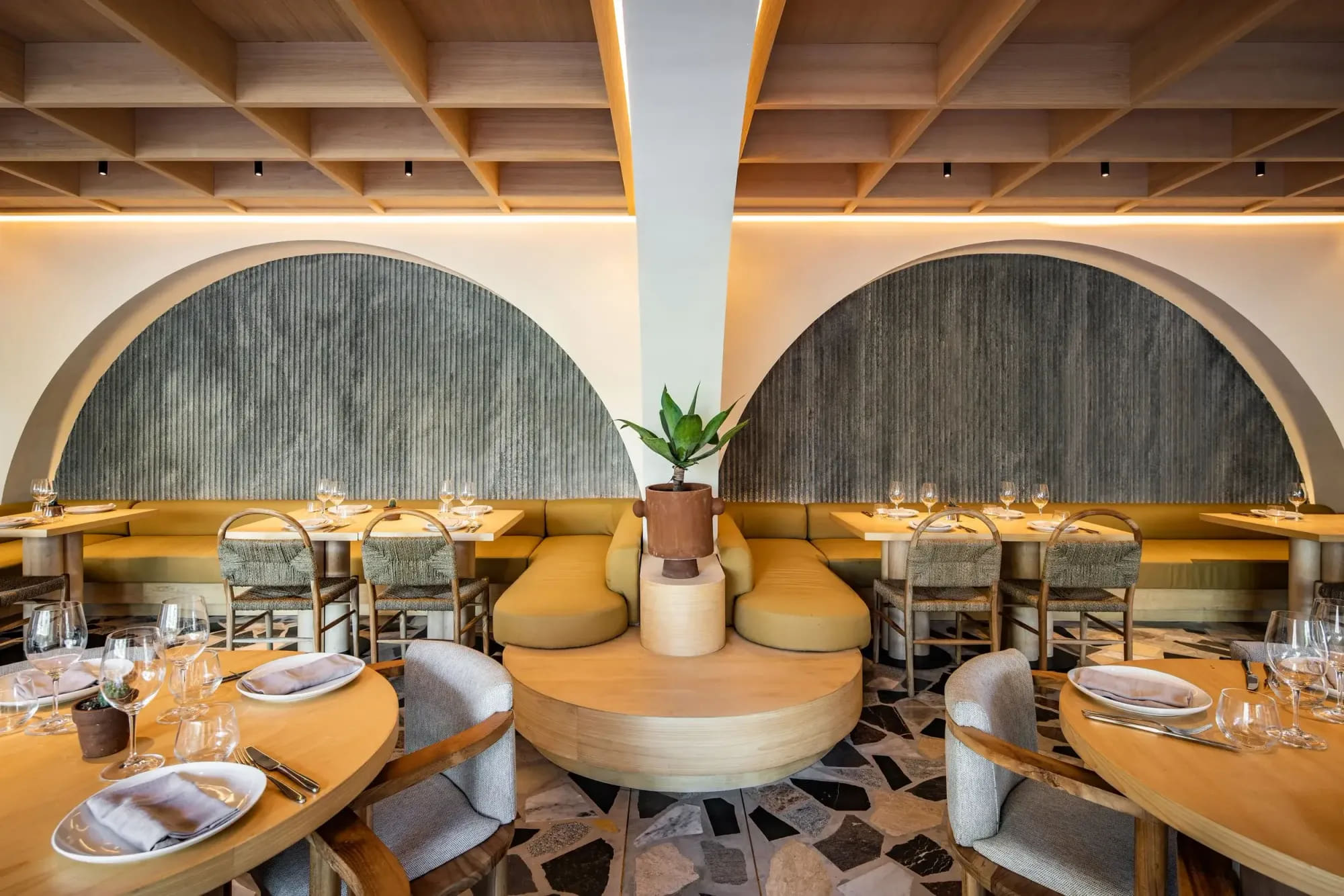 Luma's dining room: twin fluted-plaster arches, a timber coffered ceiling, mustard banquettes and a broken-marble terrazzo floor, tables set for service